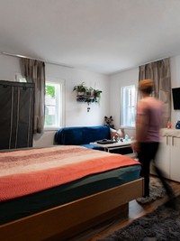 Gemütliches Zuhause für Mitarbeiter Die Mitarbeiterunterkunft des Hotel Valavier bietet einen hellen Wohnbereich mit Bett, Sofa und Fernseher. Eine Person bewegt sich durch den gemütlich eingerichteten Raum.