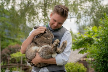 Gastgeber Fabian hält einen großen Hasen im Arm und streichelt ihn liebevoll. Im Hintergrund ist der grüne Garten des Hotels Valavier im Brandnertal zu sehen.