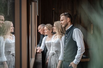 Die Gastgeberfamilie des Hotels Valavier steht gemeinsam am Fenster und blickt freundlich und aufmerksam nach draußen.
