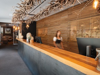 Herzlichkeit am Empfang Eine Mitarbeiterin steht hinter der Rezeption des Hotel Valavier und ist mitten im Arbeitsalltag. Der Empfangsbereich ist mit warmen Holzelementen und natürlichen Details gestaltet.