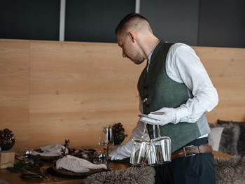 Service mit Herz und Qualität Ein Mitarbeiter des Hotel Valavier trägt mehrere Gläser und bereitet den Restauranttisch für die Gäste vor.
