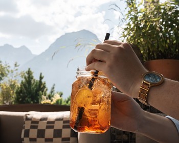 Erfrischung mit Bergblick Eine Person genießt ein erfrischendes Getränk mit Zitronenscheiben auf der Terrasse. Im Hintergrund eröffnet sich der Blick auf die beeindruckende Bergwelt des Brandnertals.