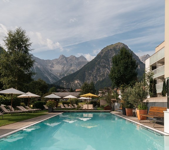 Ein großzügiger Außenpool des Hotel Valavier lädt zum Entspannen und Erholen ein. Im Hintergrund eröffnet sich ein beeindruckendes Bergpanorama des Brandnertals.