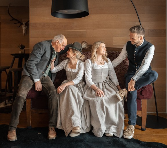 Die Gastgeberfamilie des Hotels Valavier sitzt gemeinsam auf einer gemütlichen Bank und tauscht sich herzlich aus. Alle vier tragen traditionelle Tracht und vermitteln ein familiäres und herzliches Miteinander.